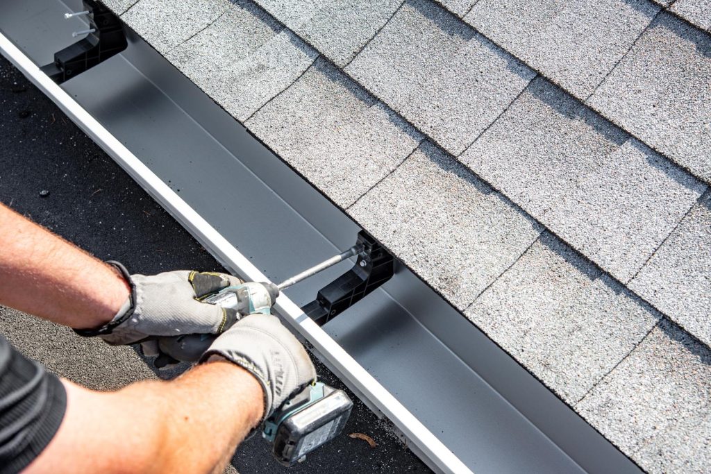 Installer fastening a durable seamless gutter system to a roofline.